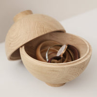 Natural wood grain bowl with a smooth beige finish, showcasing a collection of colorful patterned bangles inside.