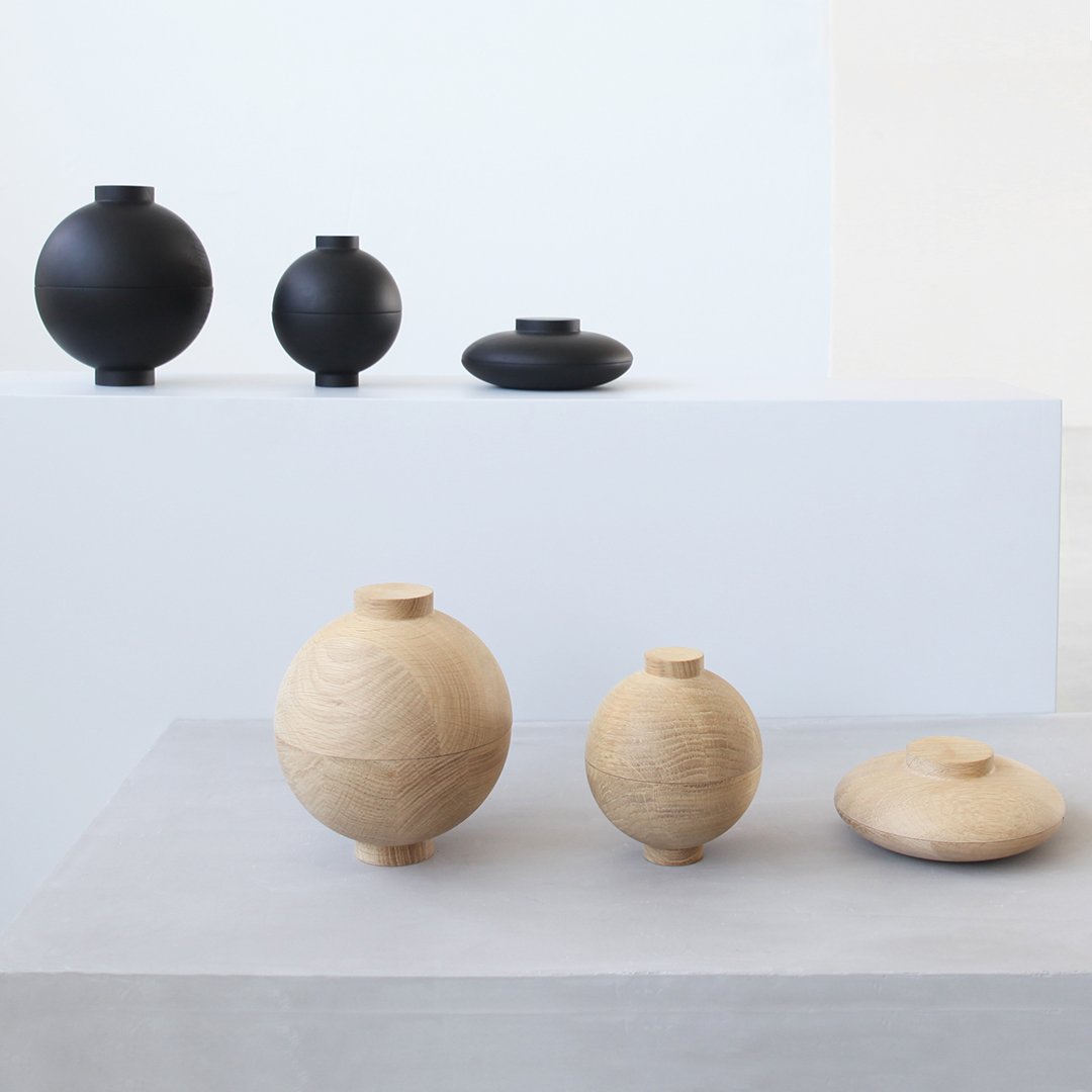Set of minimalist wooden vases in natural wood tones and matte black, featuring smooth, spherical shapes and clean lines.