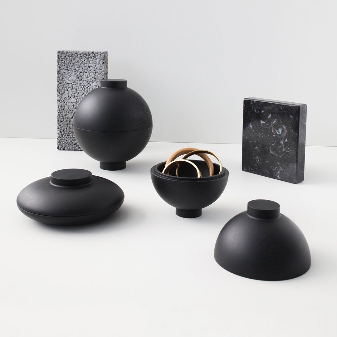 Black ceramic vases and bowls with smooth finishes, complemented by black and white patterned decorative objects.