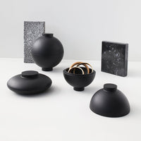 Collection of matte black decorative bowls and vases with abstract patterns on surrounding items.