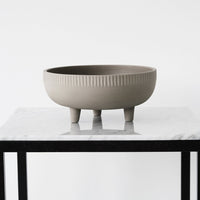 Gray ceramic bowl with textured ribbed pattern, featuring three short legs, displayed on a marble surface.