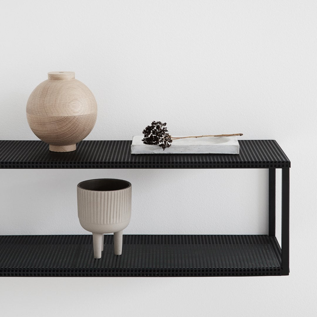 "Black shelf with natural wood vase, stone decor, and gray textured planter, showcasing minimalist design."
