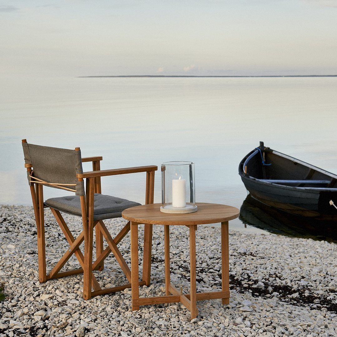 Wooden chair and table set in natural tones, featuring gray fabric upholstery and a serene coastal backdrop.