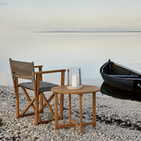 Wooden chair and table set in natural tones, featuring gray fabric upholstery and a serene coastal backdrop.