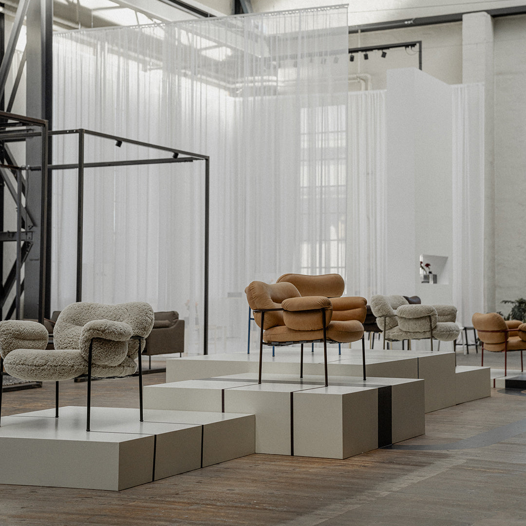 Mid-century modern chairs in soft beige and tan hues, elegantly displayed on clean white pedestals against a minimalist backdrop.
