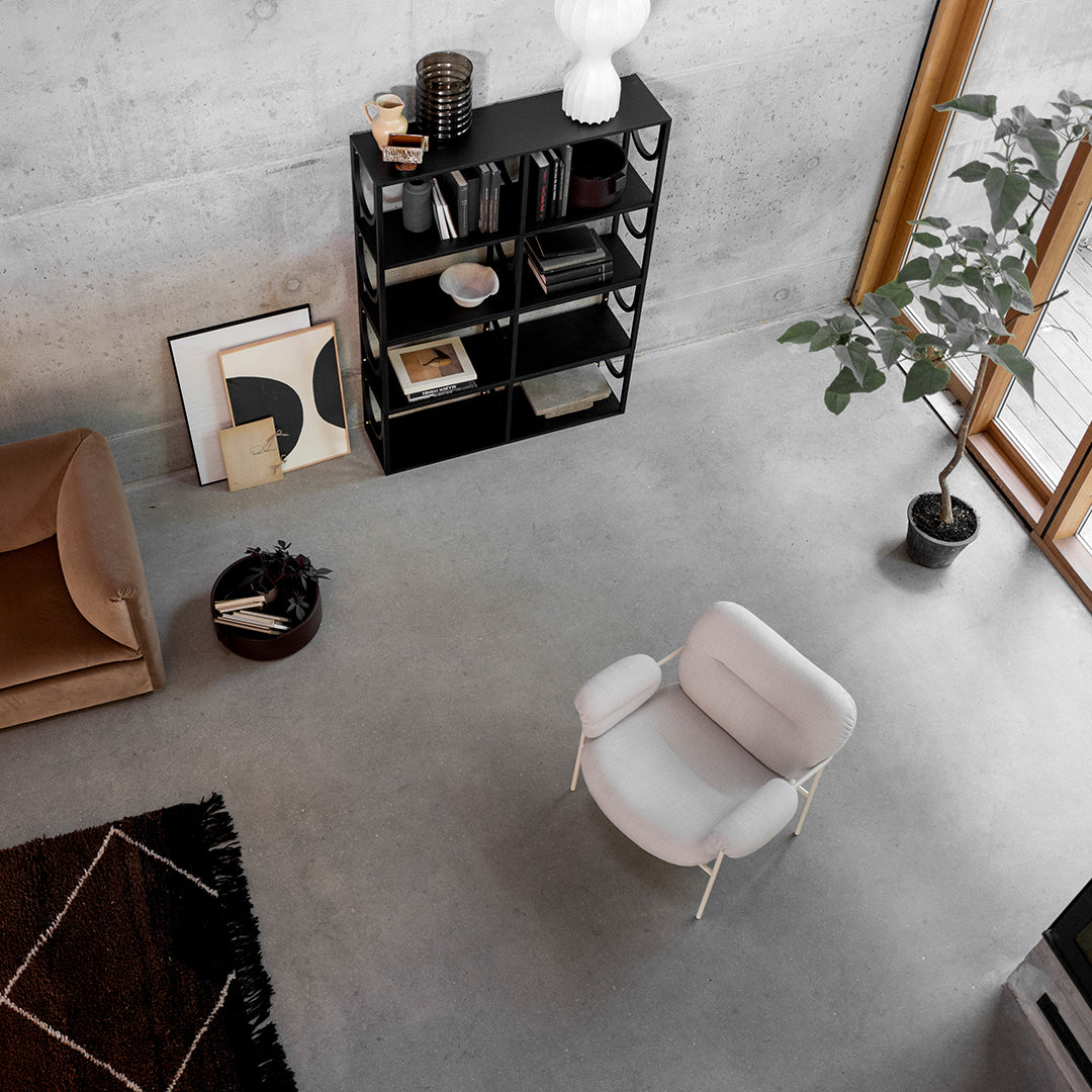 Cozy white armchair on gray floor, surrounded by earthy tones, black shelves, and a black and white patterned rug.