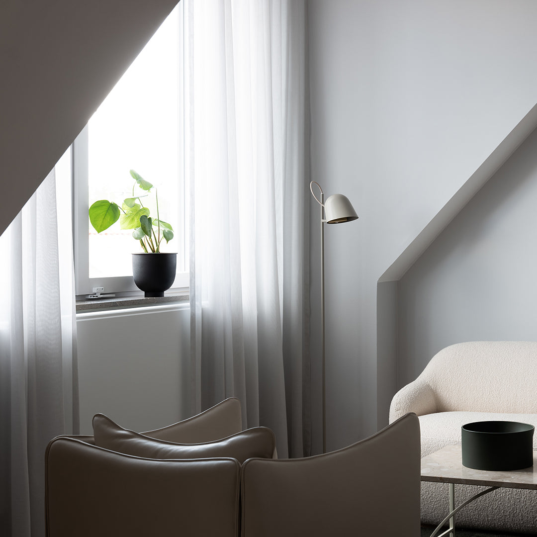 "Light gray walls, sheer white curtains, beige furniture, and a black accent planter create a modern, neutral interior."
