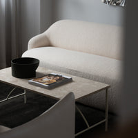 Light beige textured sofa with a neutral color palette, paired with a black bowl and a stylish magazine on a light table.