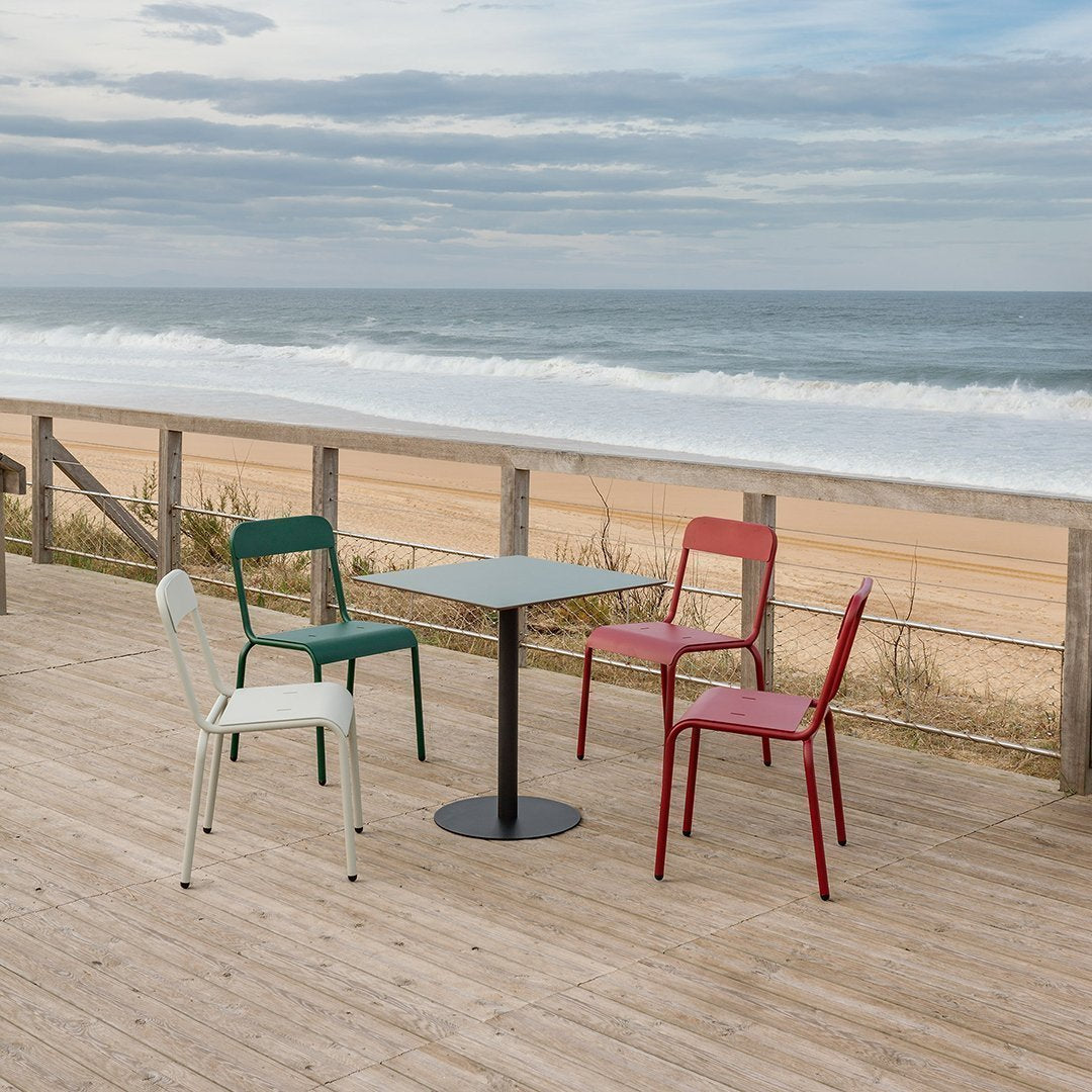 Colorful outdoor cafe set featuring red, green, and white chairs around a sleek black table with ocean backdrop.