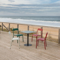 Colorful outdoor cafe set featuring red, green, and white chairs around a sleek black table with ocean backdrop.