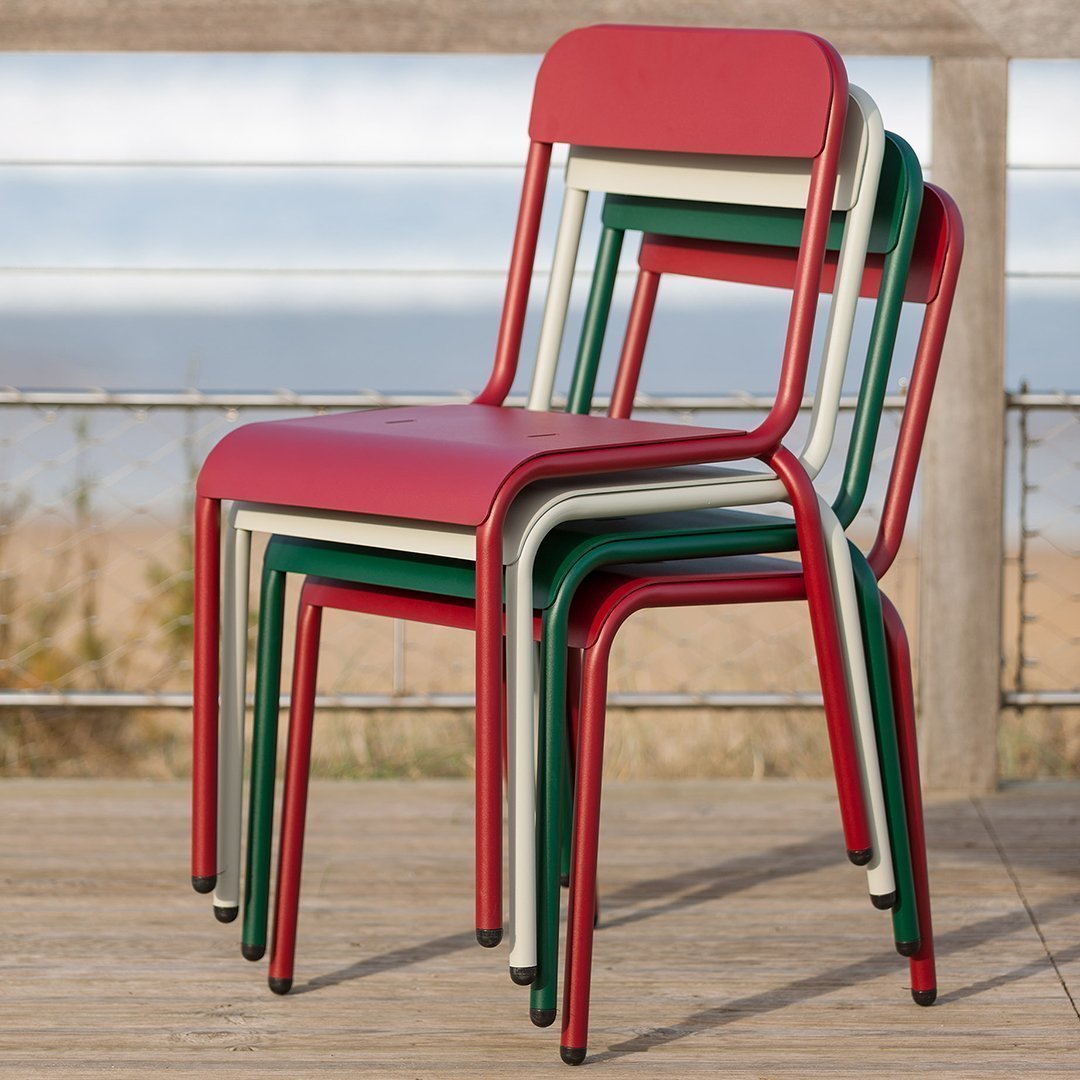 Stacked chairs featuring red, green, and cream colors with a sleek design, set against a natural background.