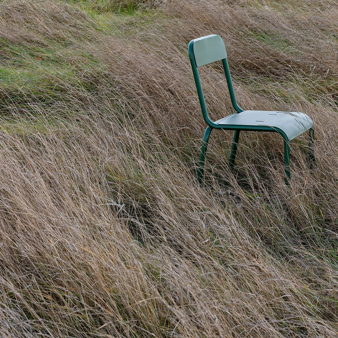Green metal chair on a textured backdrop of dry, golden grass. Ideal for rustic or outdoor decor styling.