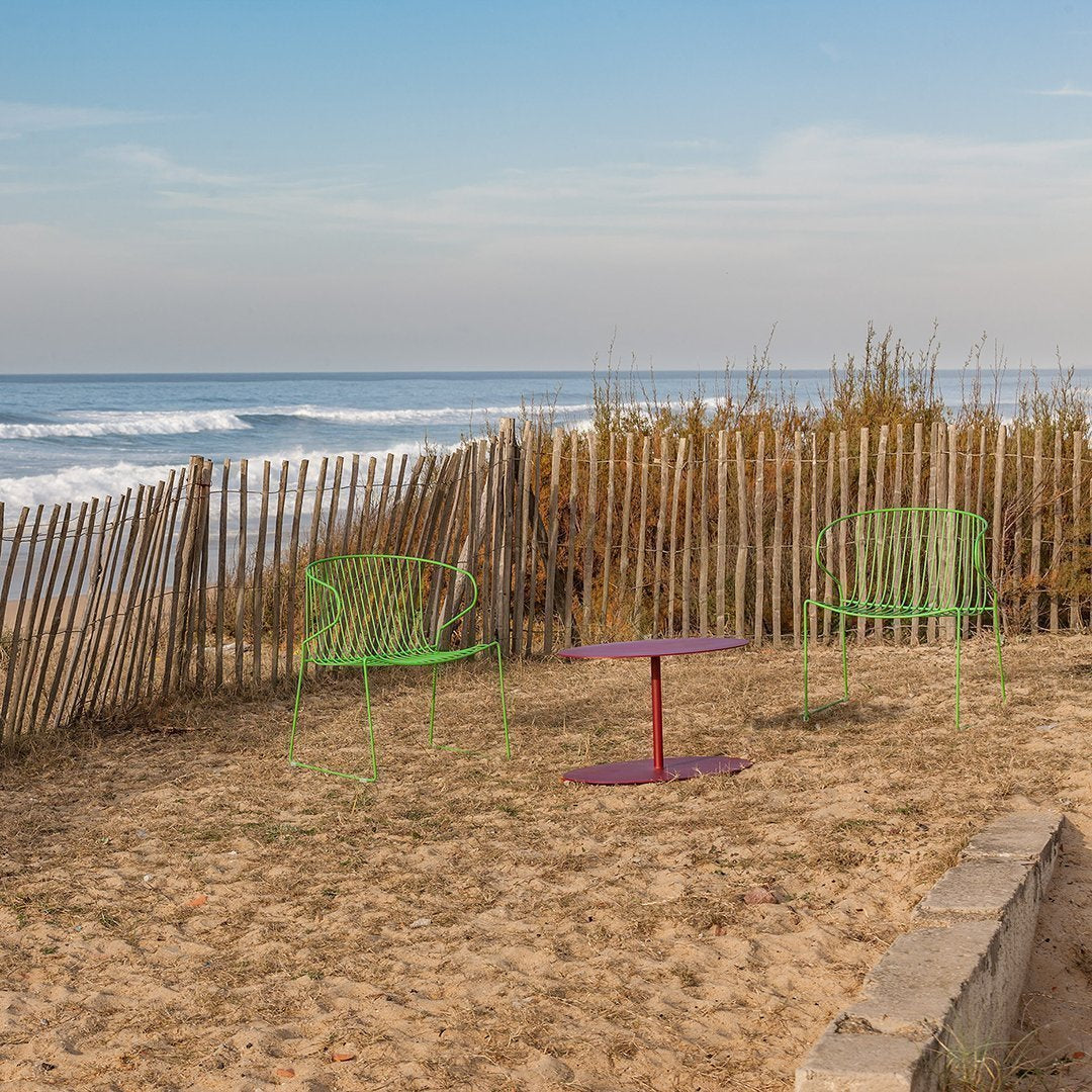 "Vibrant green chairs with a purple table against a sandy beach backdrop, complemented by blue ocean and clear sky."