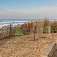 "Vibrant green chairs with a purple table against a sandy beach backdrop, complemented by blue ocean and clear sky."