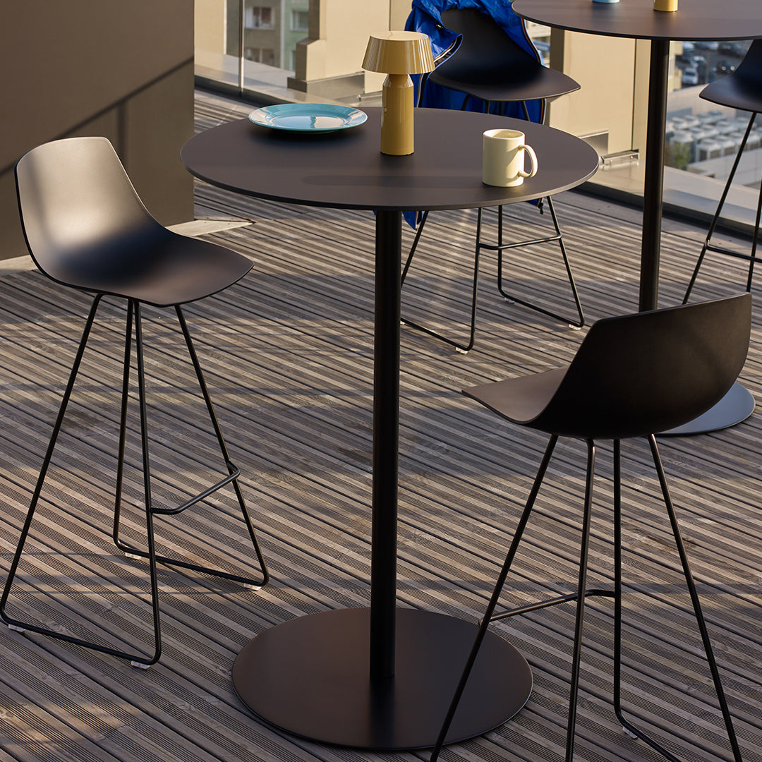 Modern black bistro table with sleek chairs on striped wooden deck, featuring a blue plate and a yellow lamp.