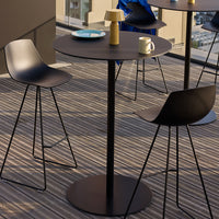 Modern black bistro table with sleek chairs on striped wooden deck, featuring a blue plate and a yellow lamp.