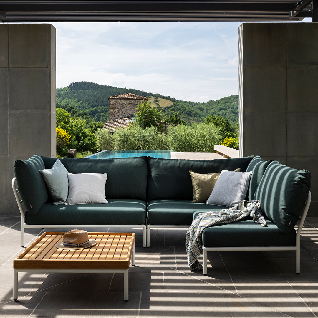 Teal sectional sofa with white accents, complemented by neutral pillows and a wooden coffee table against a scenic backdrop.