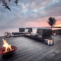Modern outdoor seating in charcoal gray, accented by soft cushions, with a warm fire pit and serene lake backdrop.