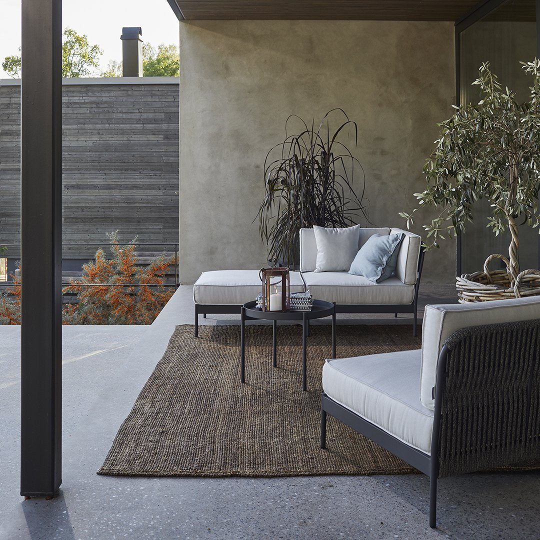 Neutral gray walls, earthy brown rug, and soft white seating with subtle blue accents create a serene outdoor space.
