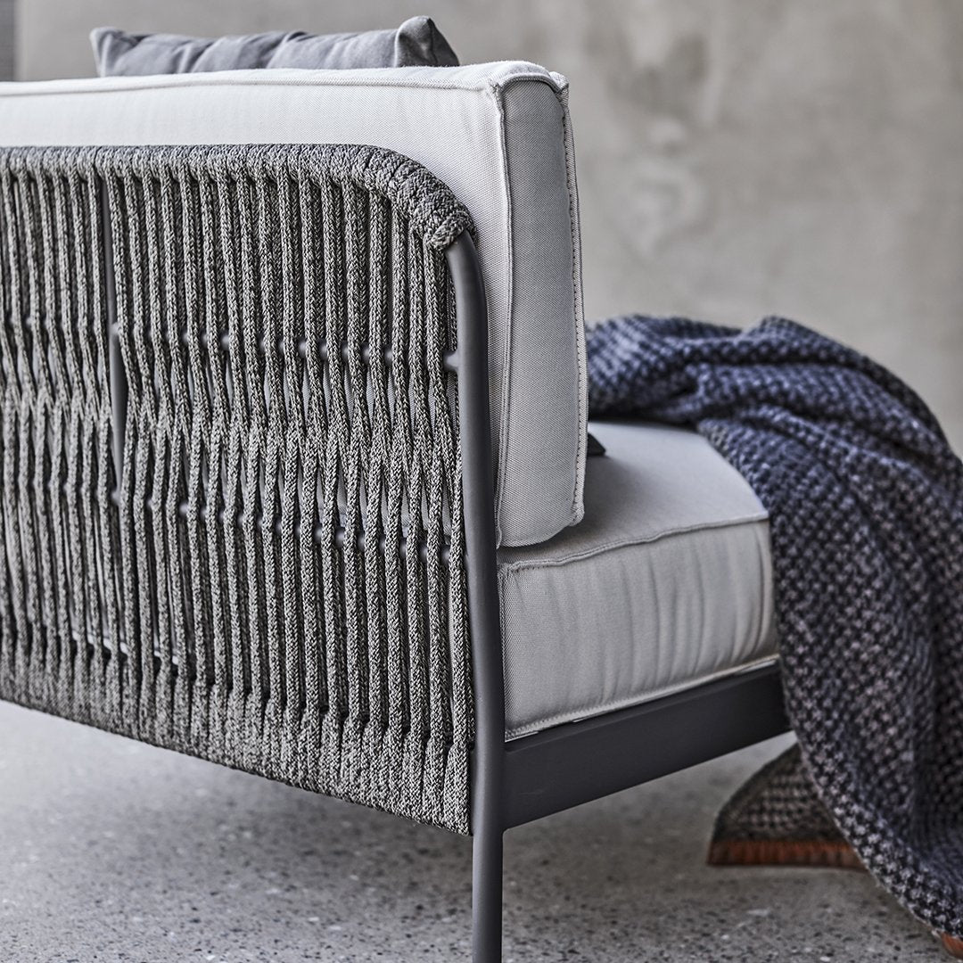 Gray woven back sofa with light gray cushions and a navy patterned throw draped over the arm. Modern decor style.