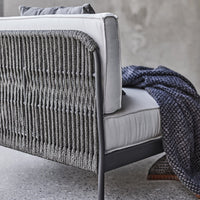 Gray woven back sofa with light gray cushions and a navy patterned throw draped over the arm. Modern decor style.