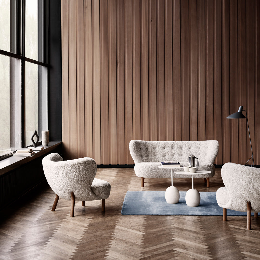 Cozy white textured upholstery on chairs and sofa, paired with a soft blue rug and warm wooden accents.