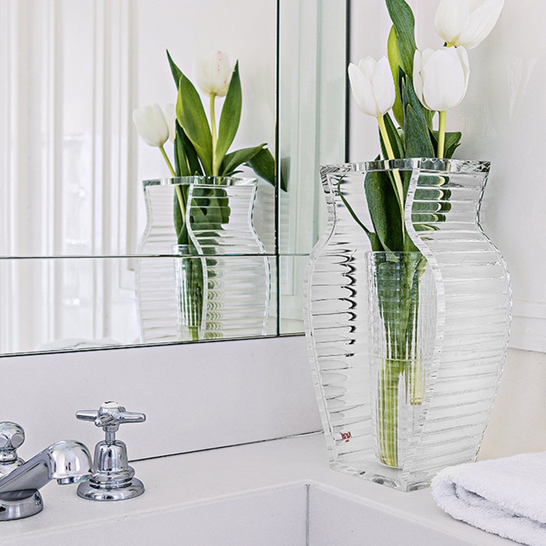 Clear ribbed glass vase with a sleek design, filled with white tulips against a bright, modern bathroom backdrop.