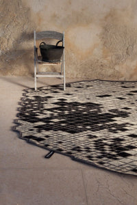 Black and white patterned rug with geometric designs, complementing the neutral backdrop and wooden chair.
