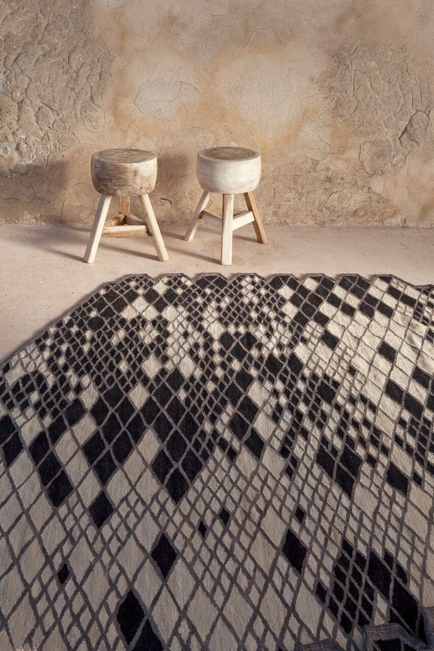 Black and white geometric patterned blanket draped over a surface, with natural wood stools in the background.