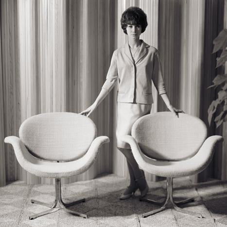 Two stylish, retro armchairs in soft cream upholstery with a round, smooth design, set against a textured background.