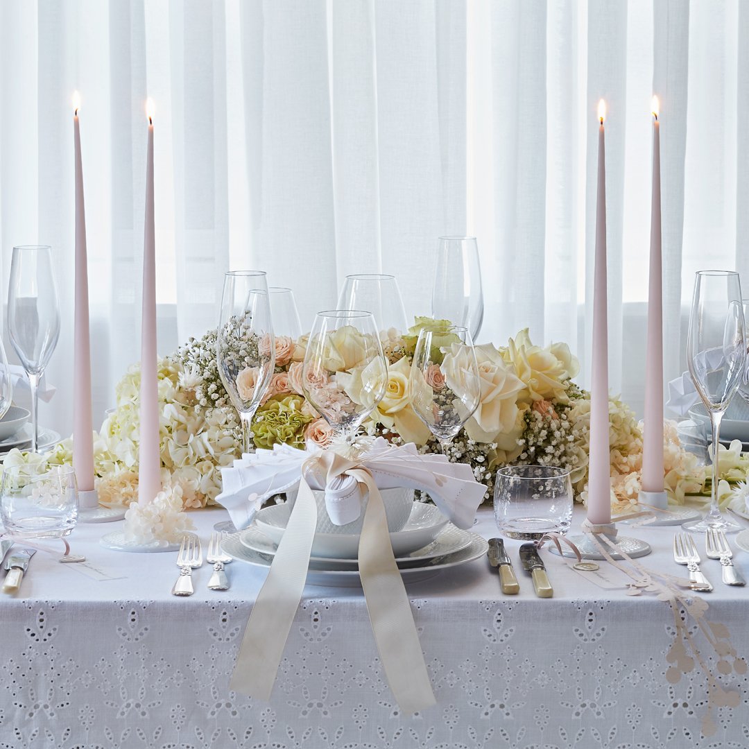 Elegant white table setting with soft pastel floral arrangements and tall, slim candles for a sophisticated look.