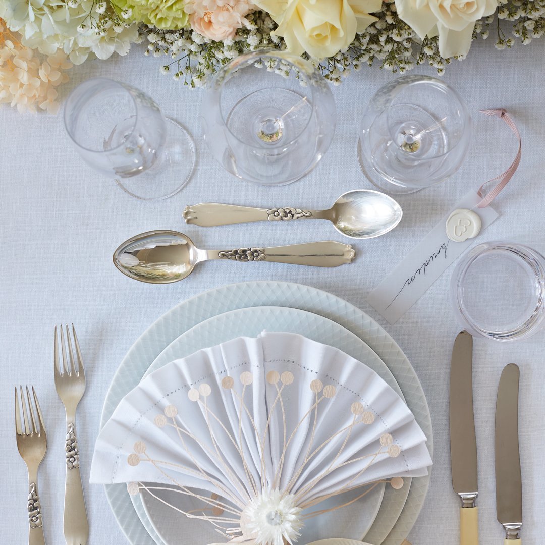 Elegant table setting featuring pastel blue plates, a white fan napkin with gold dots, and clear glassware.
