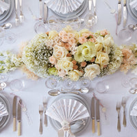 Elegant floral centerpiece featuring soft peach, cream roses, and delicate white accents on a pristine white tablecloth.