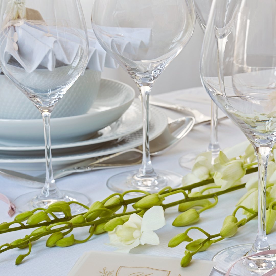 Elegant white table setting with clear glassware, soft green accents, and delicate floral arrangements.