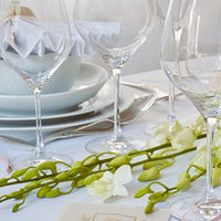 Elegant white table setting with clear glassware, soft green accents, and delicate floral arrangements.