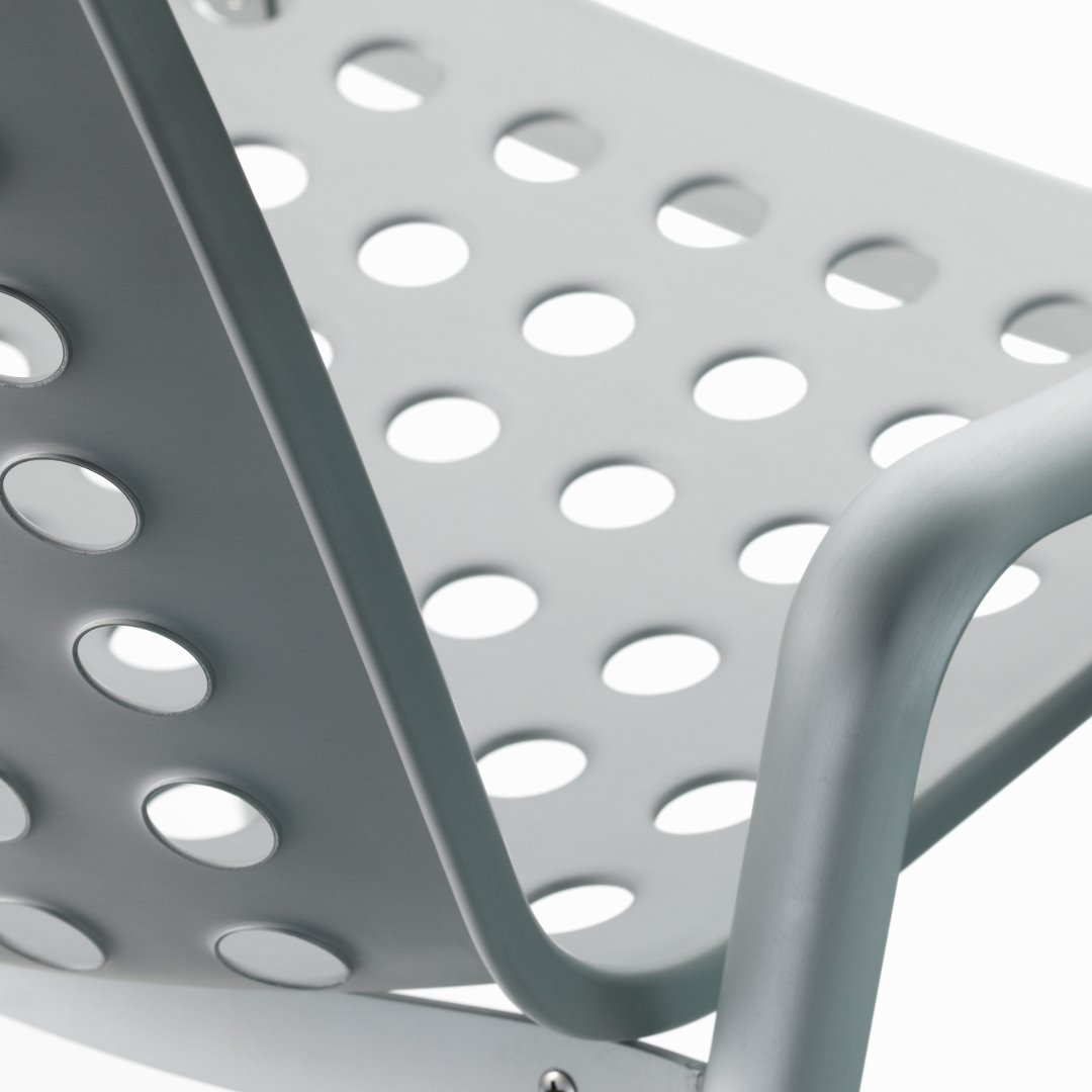 Gray metal chair with a minimalist design featuring polka dot holes for ventilation and a sleek modern look.