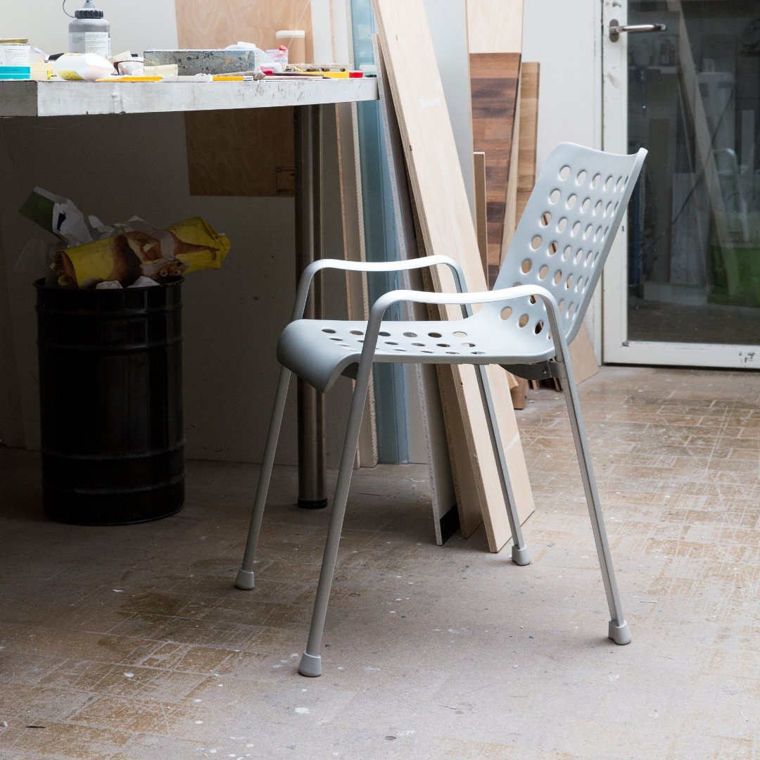 Grey perforated dining chair with smooth, sleek lines and modern design, set against a minimalistic workspace background.