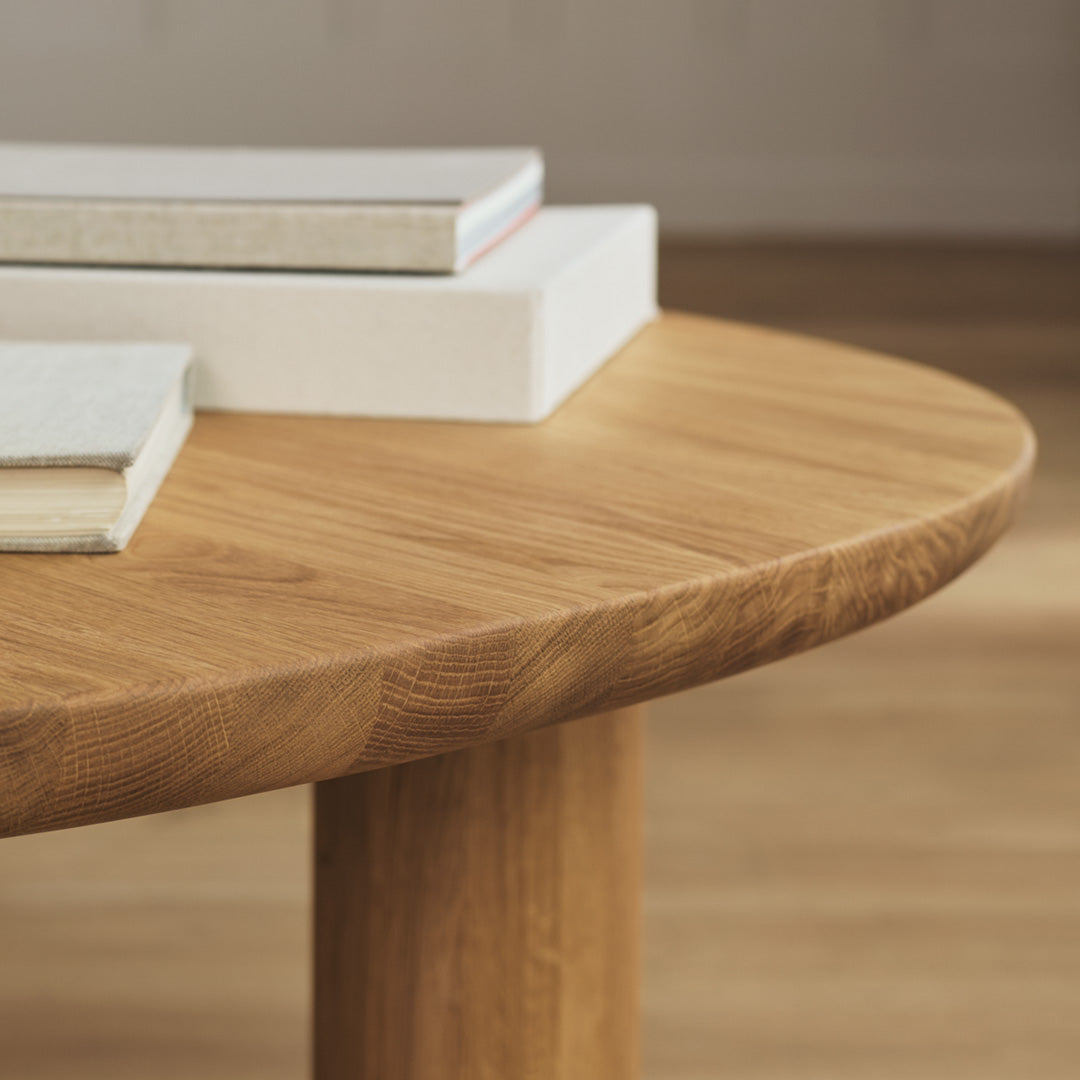 Natural oak wood table with a smooth, rounded surface and subtle grain patterns, complemented by stacked neutral-colored books.
