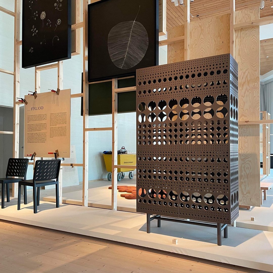 Black perforated cabinet with circular patterns, set against a light wood and neutral background, showcasing modern design.