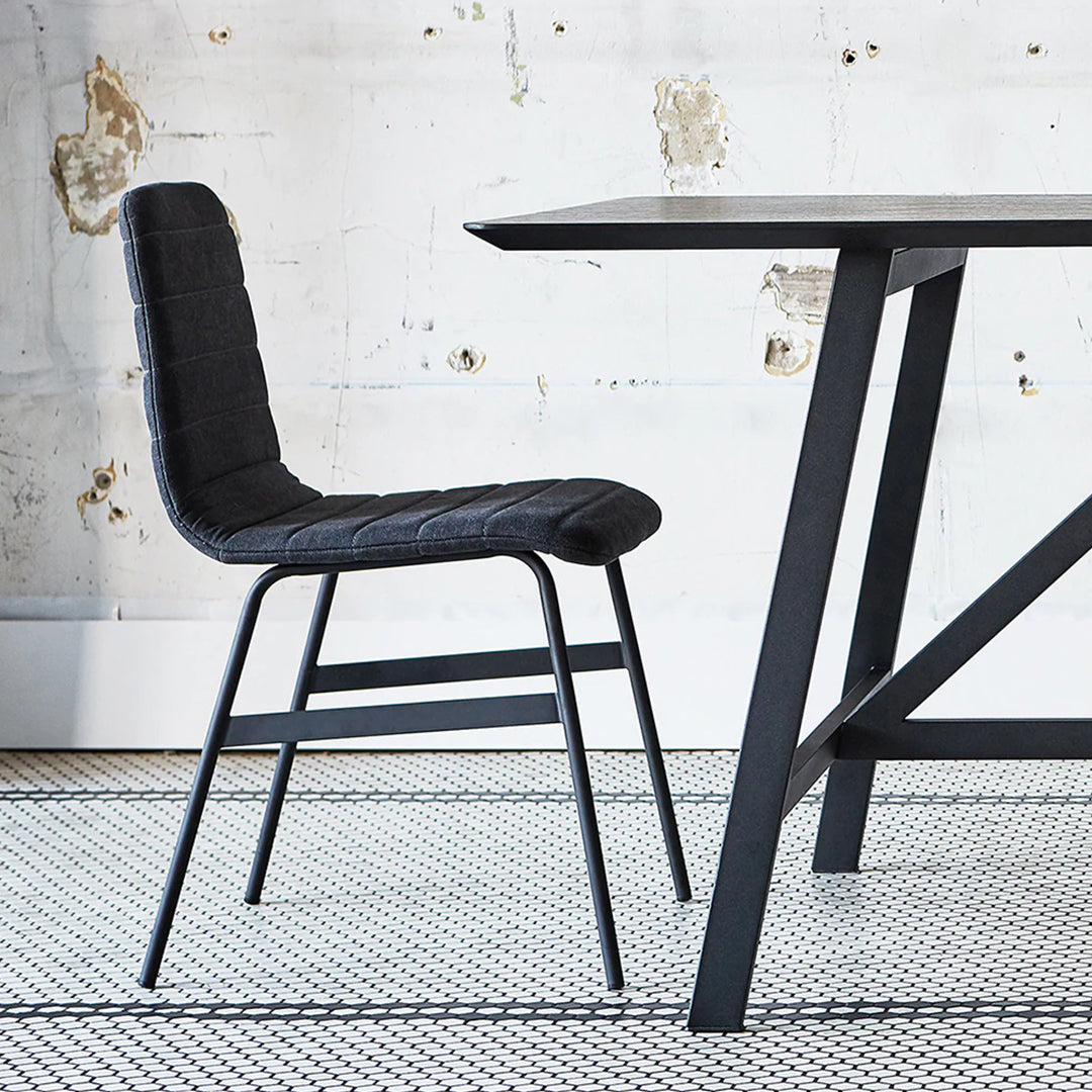 Black quilted dining chair with a minimalist design, paired with a sleek black table on a textured white patterned rug.