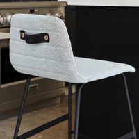 Light gray upholstered chair with a textured pattern and black metal frame, featuring a unique leather handle on the back.