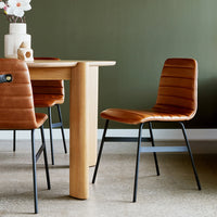 Brown ribbed chairs with black metal legs paired with a light wooden table against a green wall. Cozy and modern decor.