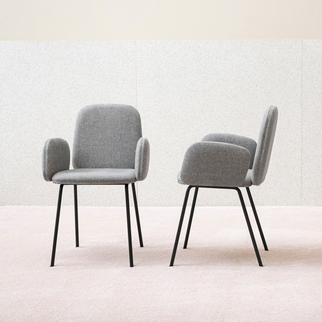 Grey upholstered chairs with rounded arms and black metal legs, set against a soft pink floor.