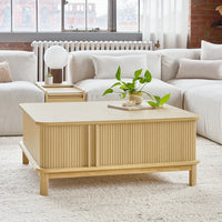 Light wood coffee table with a ribbed pattern, surrounded by soft, neutral-toned furniture and a green plant.