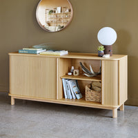 Light wood sideboard with ribbed texture, set against a warm olive green wall. Simple, modern decor accents.