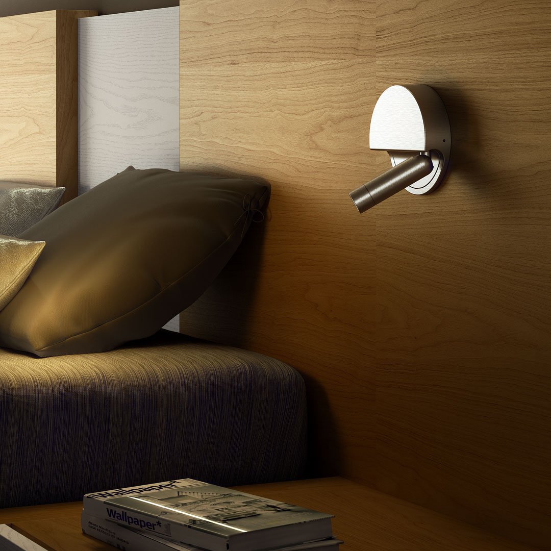 Sleek chrome wall lamp against natural wood backdrop with neutral gray pillows and a dark blue bed cover.