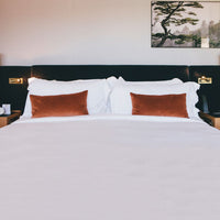 White bedding with orange accent pillows against a dark headboard, complemented by a neutral backdrop.