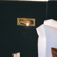 Brass accent light against a deep black backdrop, paired with soft white and brown fabric textures.
