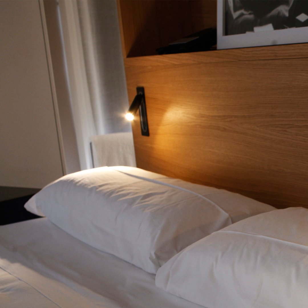Cozy white pillows on a soft white bed, accented by warm wooden tones and crisp, clean lines.