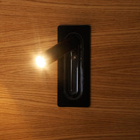 Black wall light fixture on a wooden surface, featuring a modern, minimalistic design with a sleek finish.